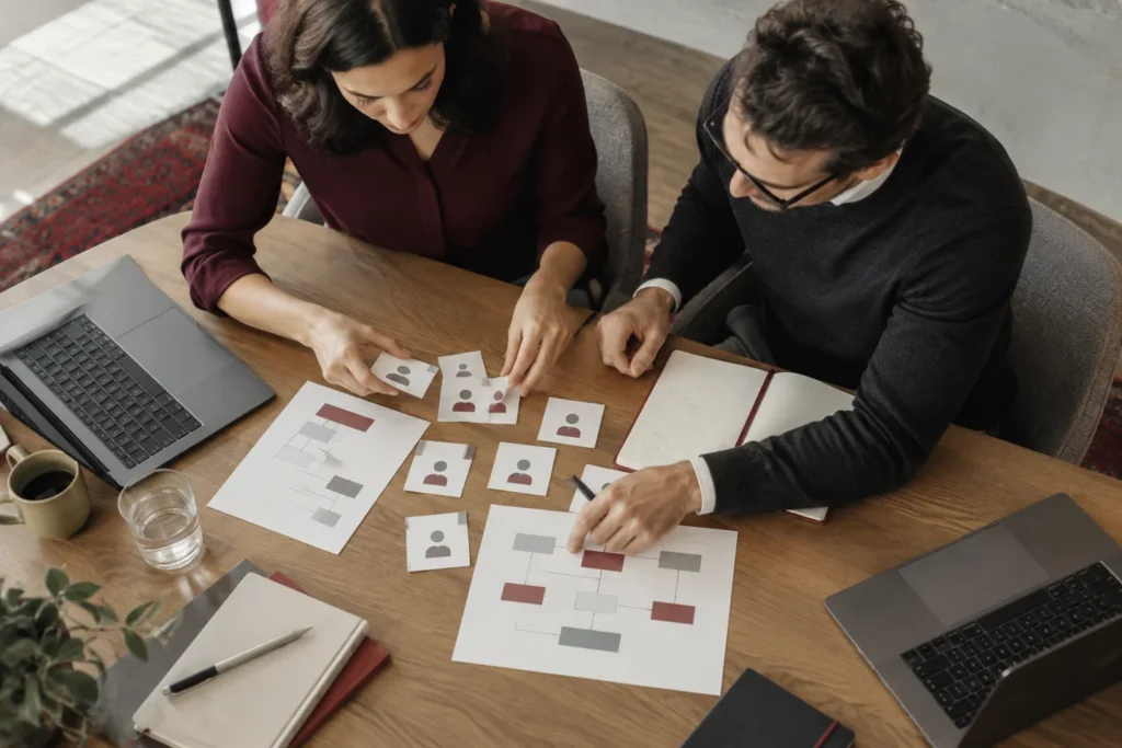 Two coworkers organizing workflow cards at a wooden table