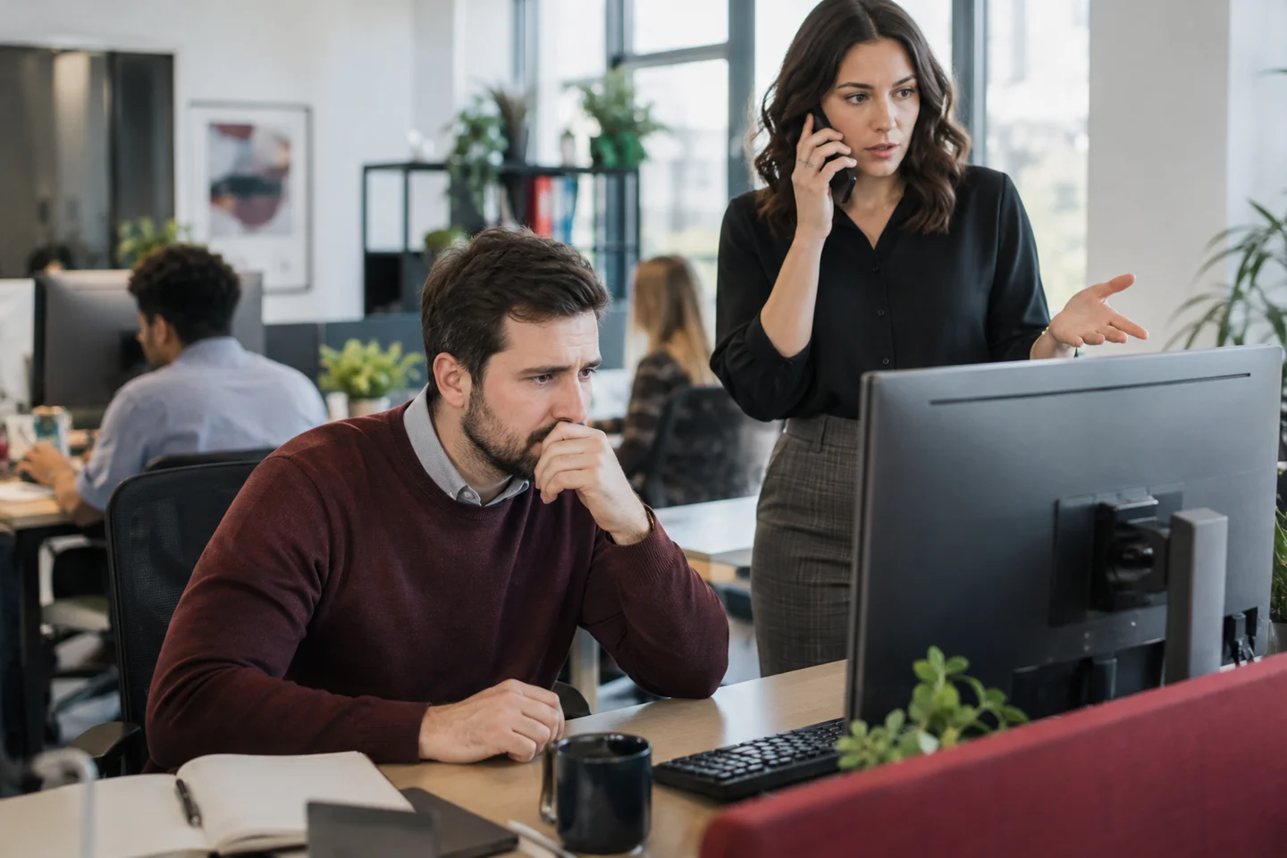 Coworkers review computer while woman takes phone call