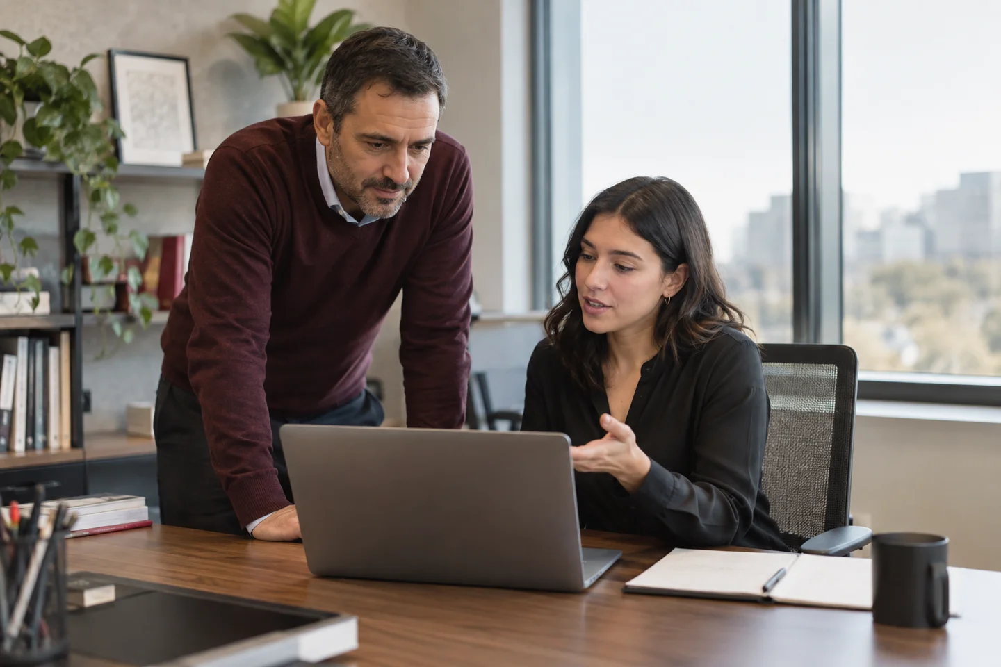 Two coworkers discuss work on a laptop in an office.
